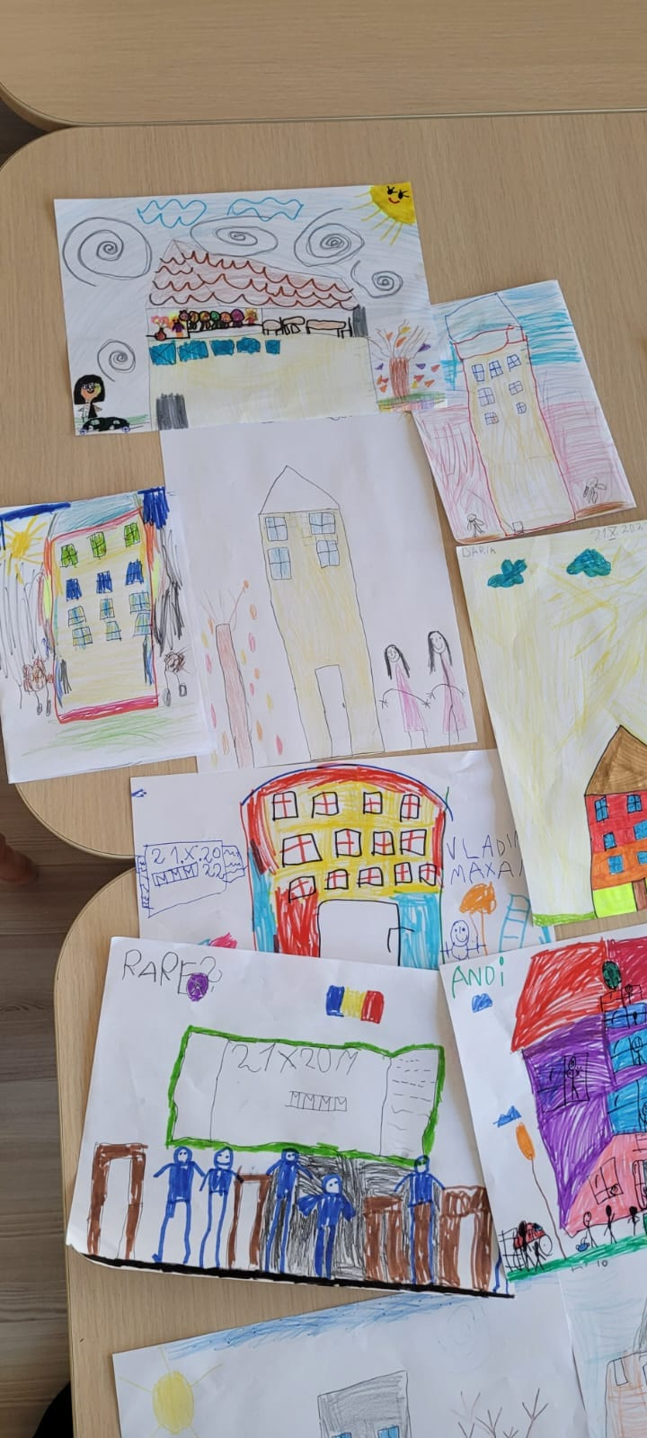 Mai multe desene despre școală realizate de elevi și prezentate pe băncile din clasă