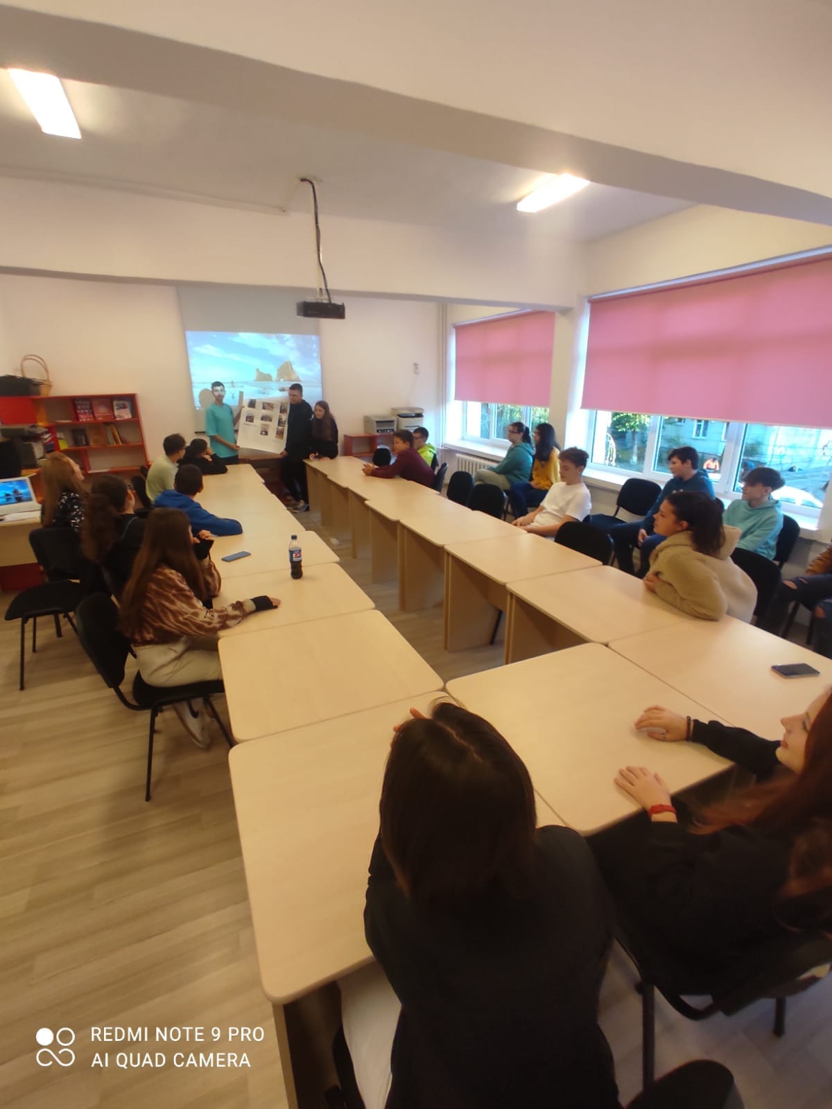 Elevi prezentând o planșă în fața clasei